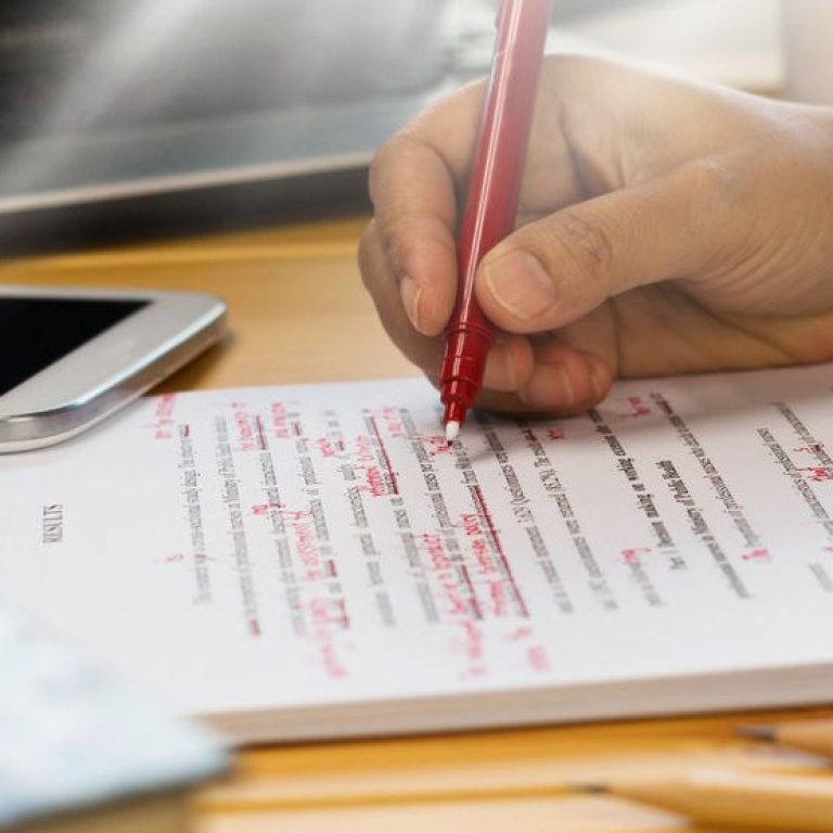 77942564 - hand holding red pen over proofreading text in office